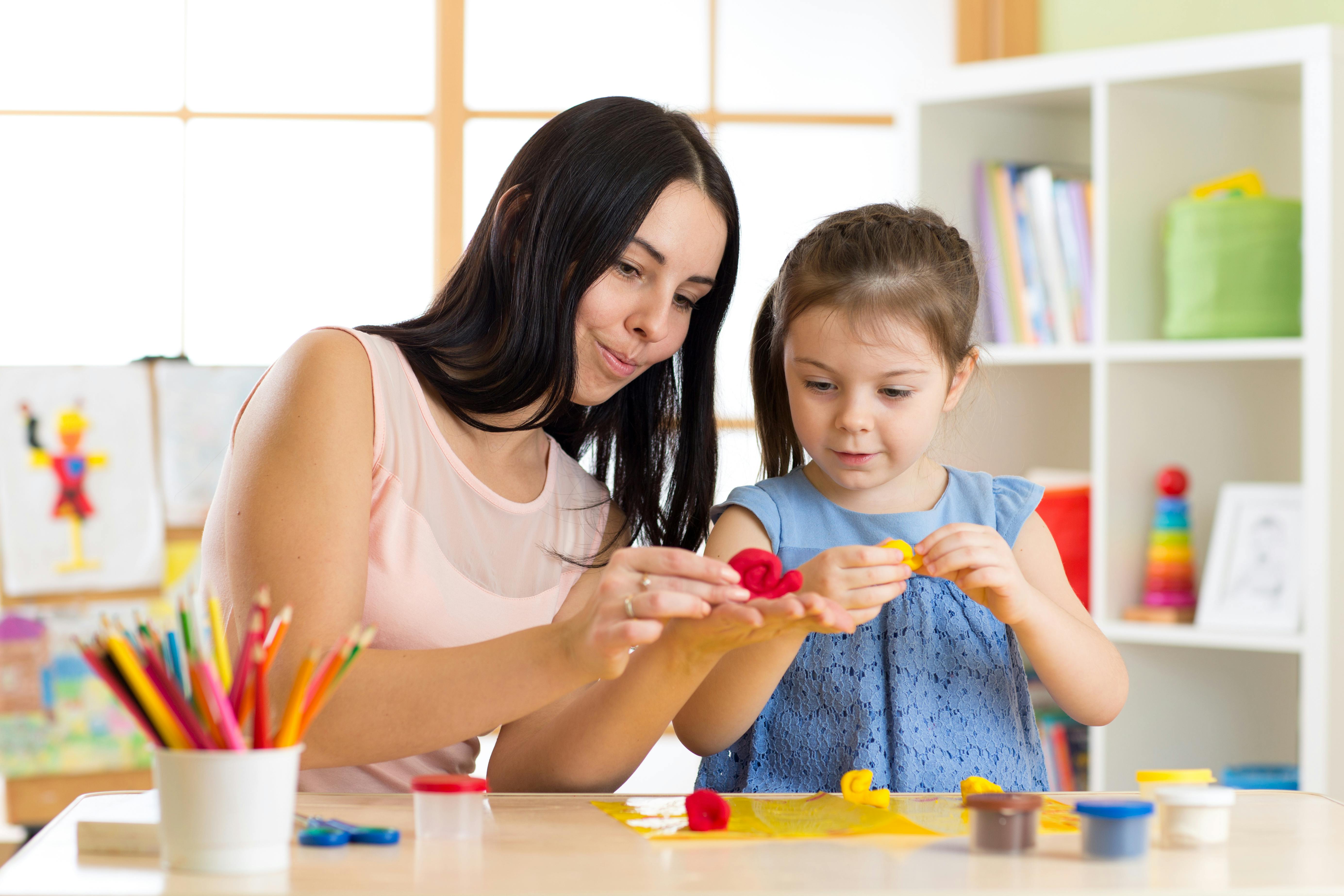 Une éducatrice aide une petite fille à modeler de la pâte à modeler, les deux concentrées sur leur activité.