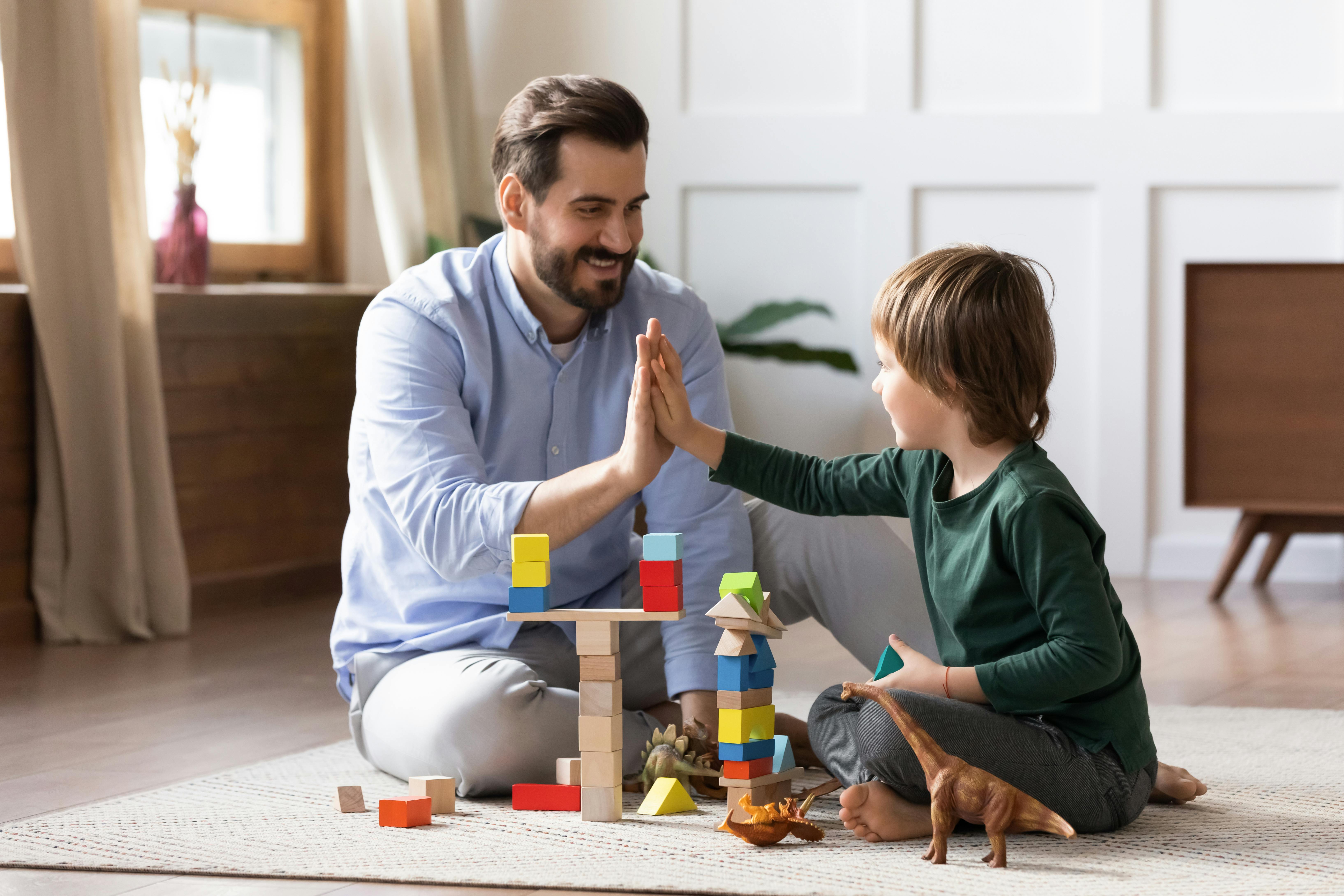 Une assistante maternelle et l'enfant qu'elle garde se font un high-five après avoir réussi une structure avec des blocs de construction en bois.
