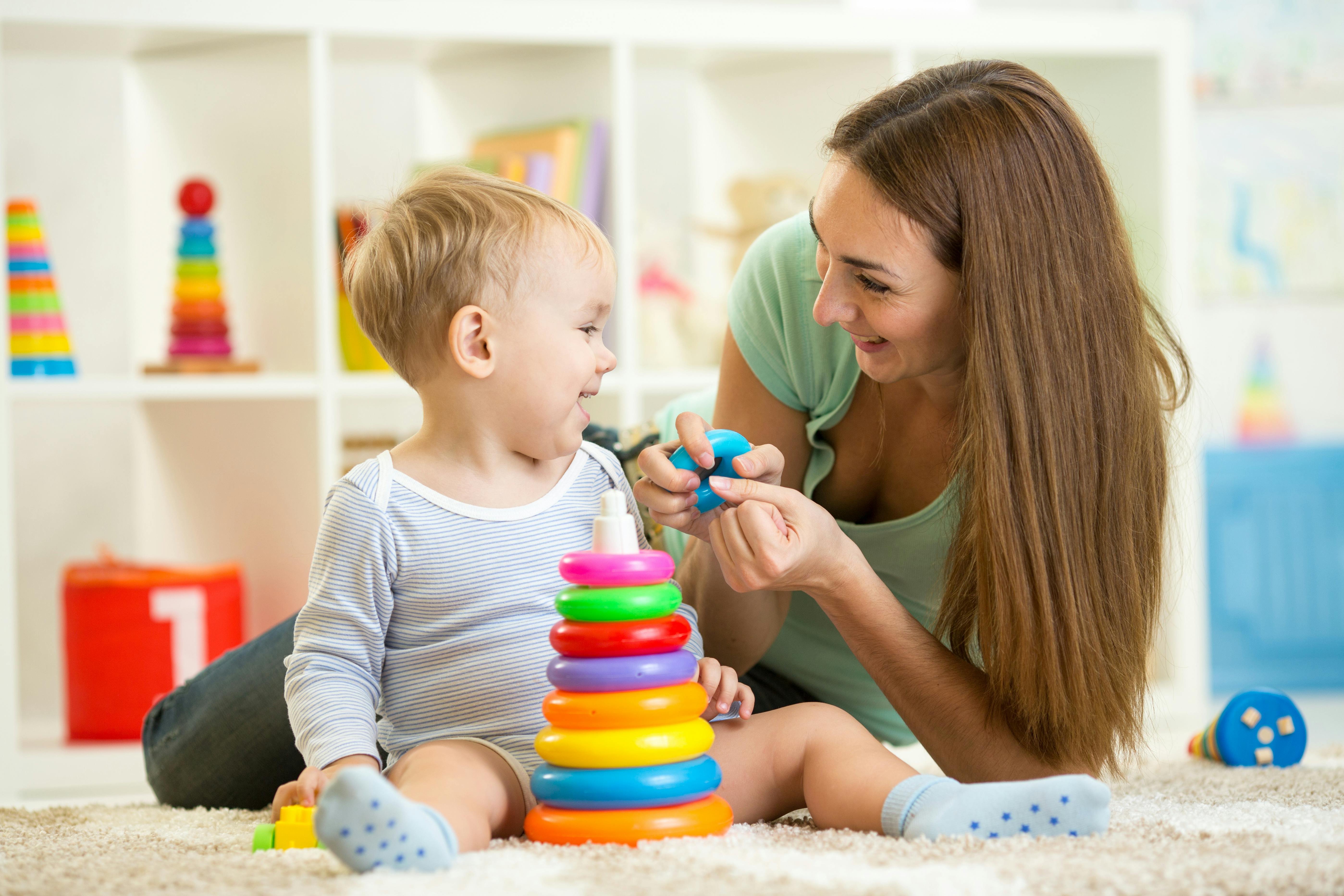 Une femme joue avec un bébé en utilisant des jouets colorés sur le sol.