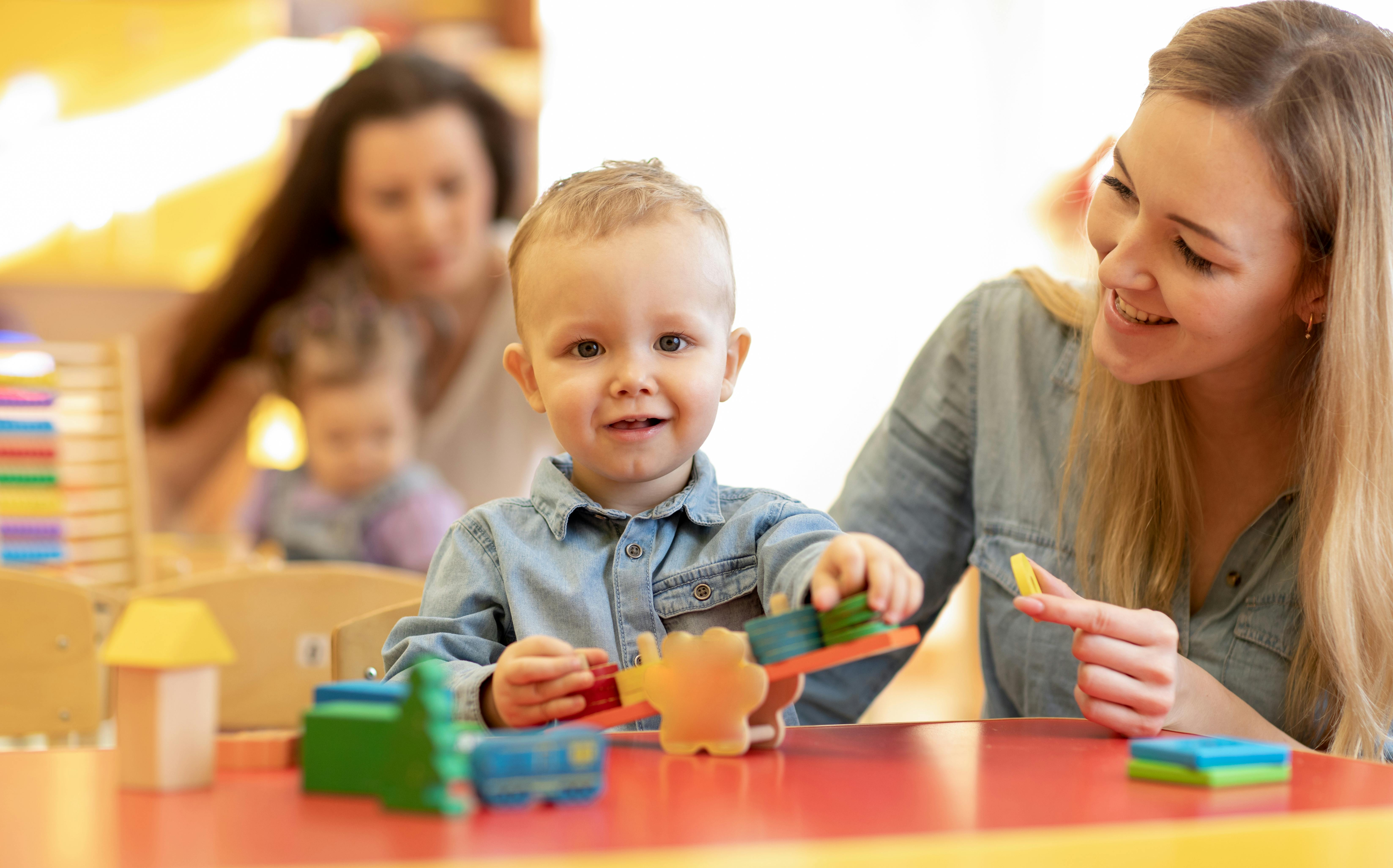 Une mère jouant avec son fils, les deux souriant et entourés de jouets colorés.