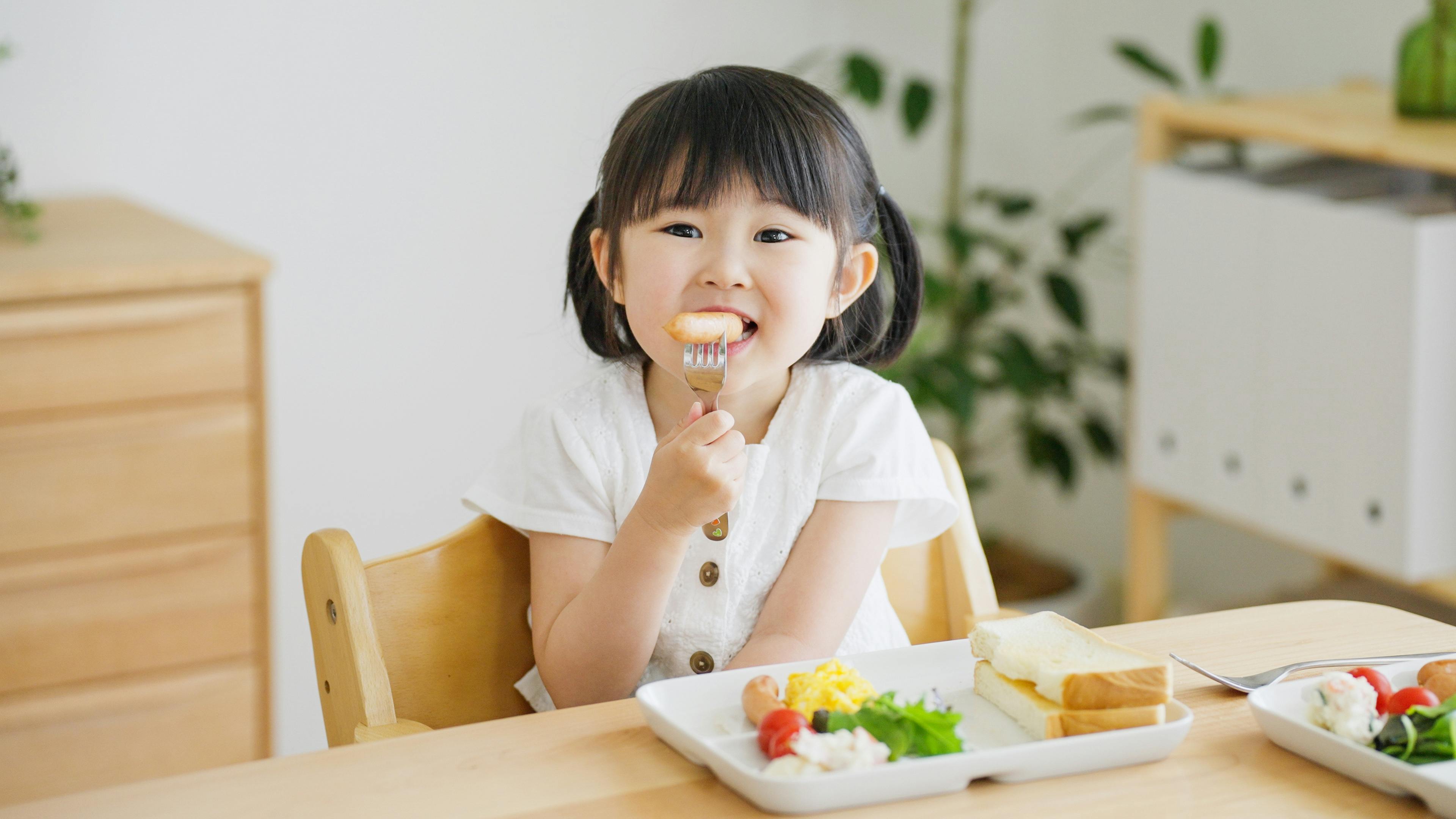 Une petite fille souriante mangeant à table avec un plateau de repas devant elle.