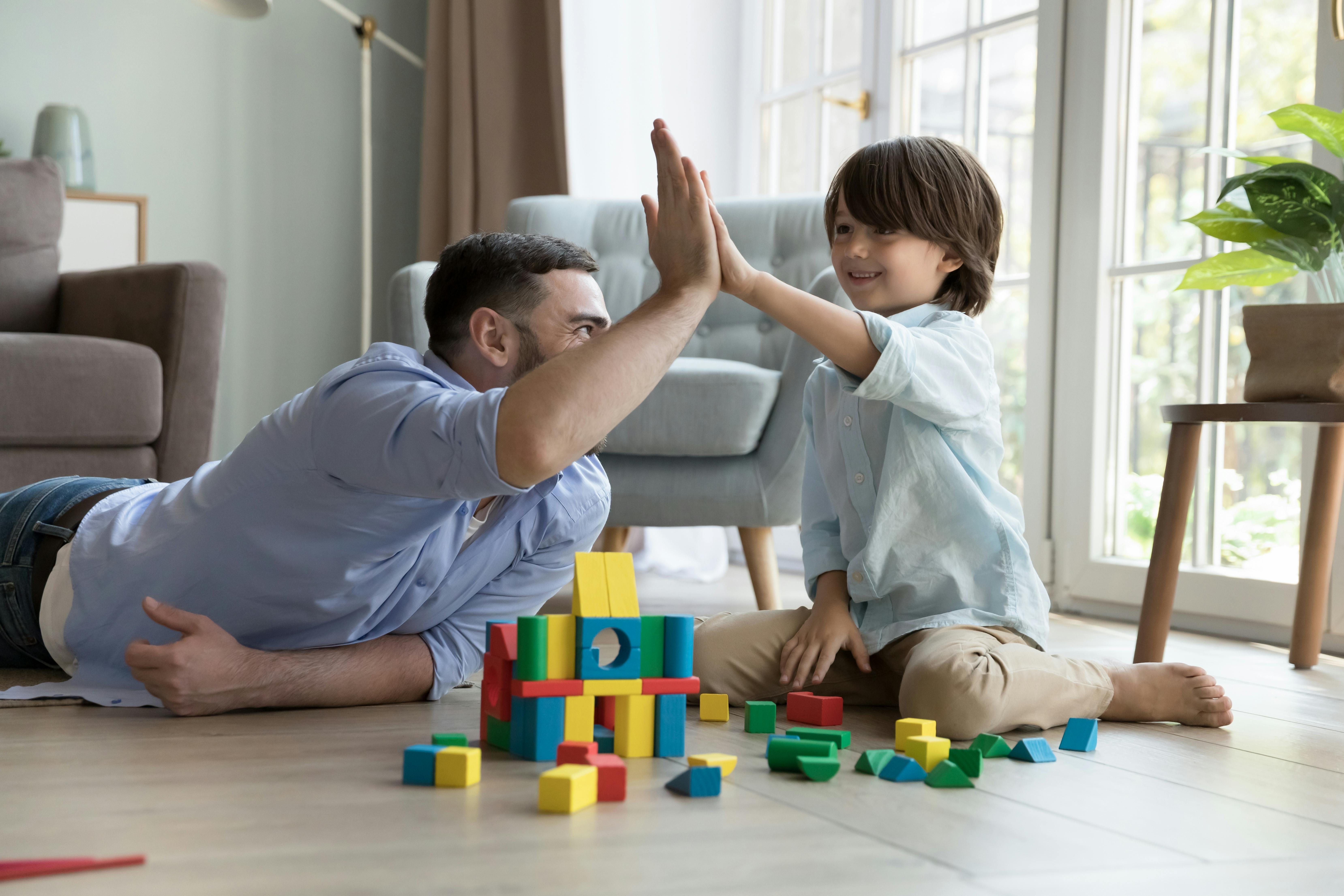 Un père et son fils se donnent un high-five après avoir construit une structure avec des blocs colorés, exprimant la joie de la réussite.