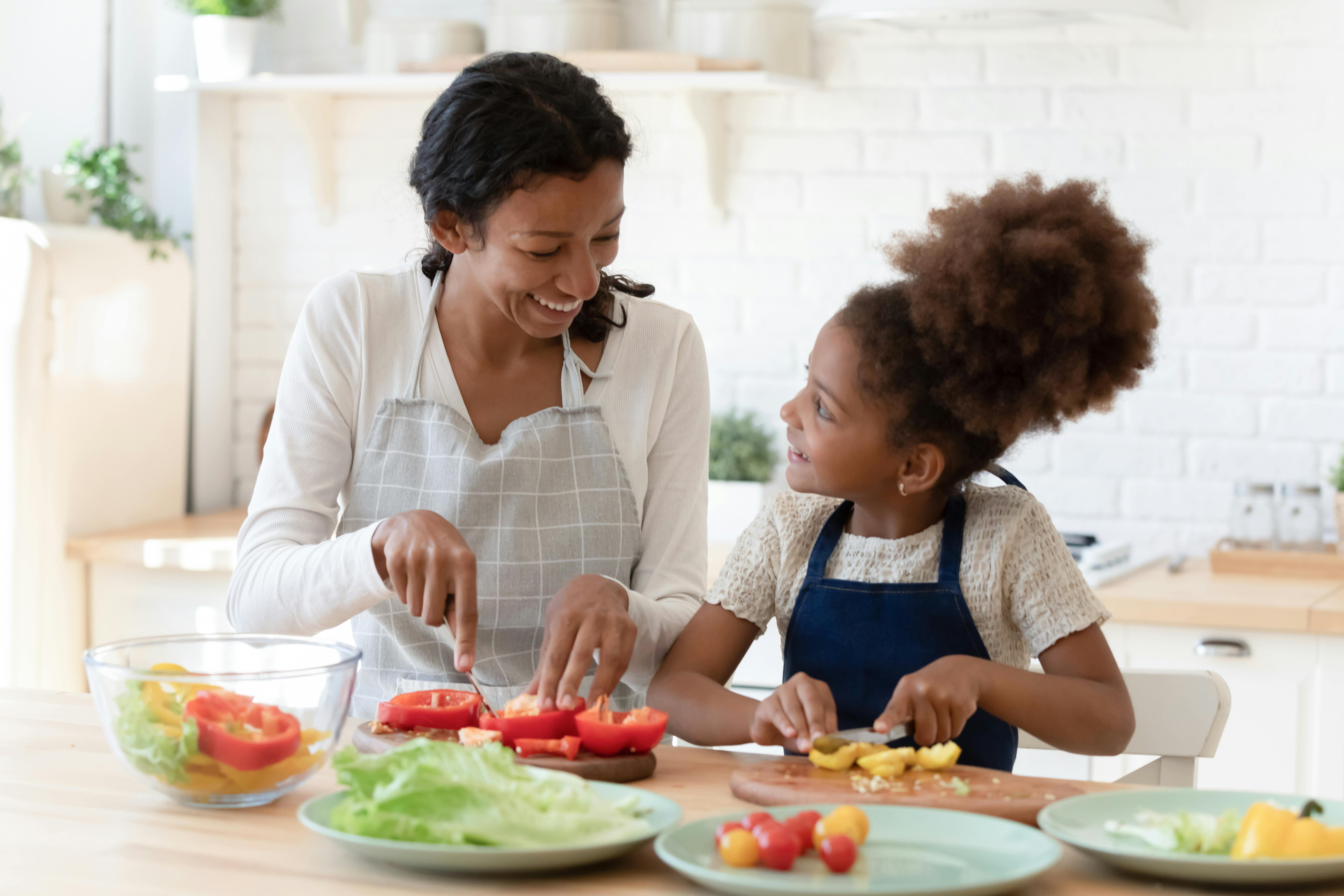 Une mère et sa fille coupant des légumes ensemble dans une cuisine lumineuse.