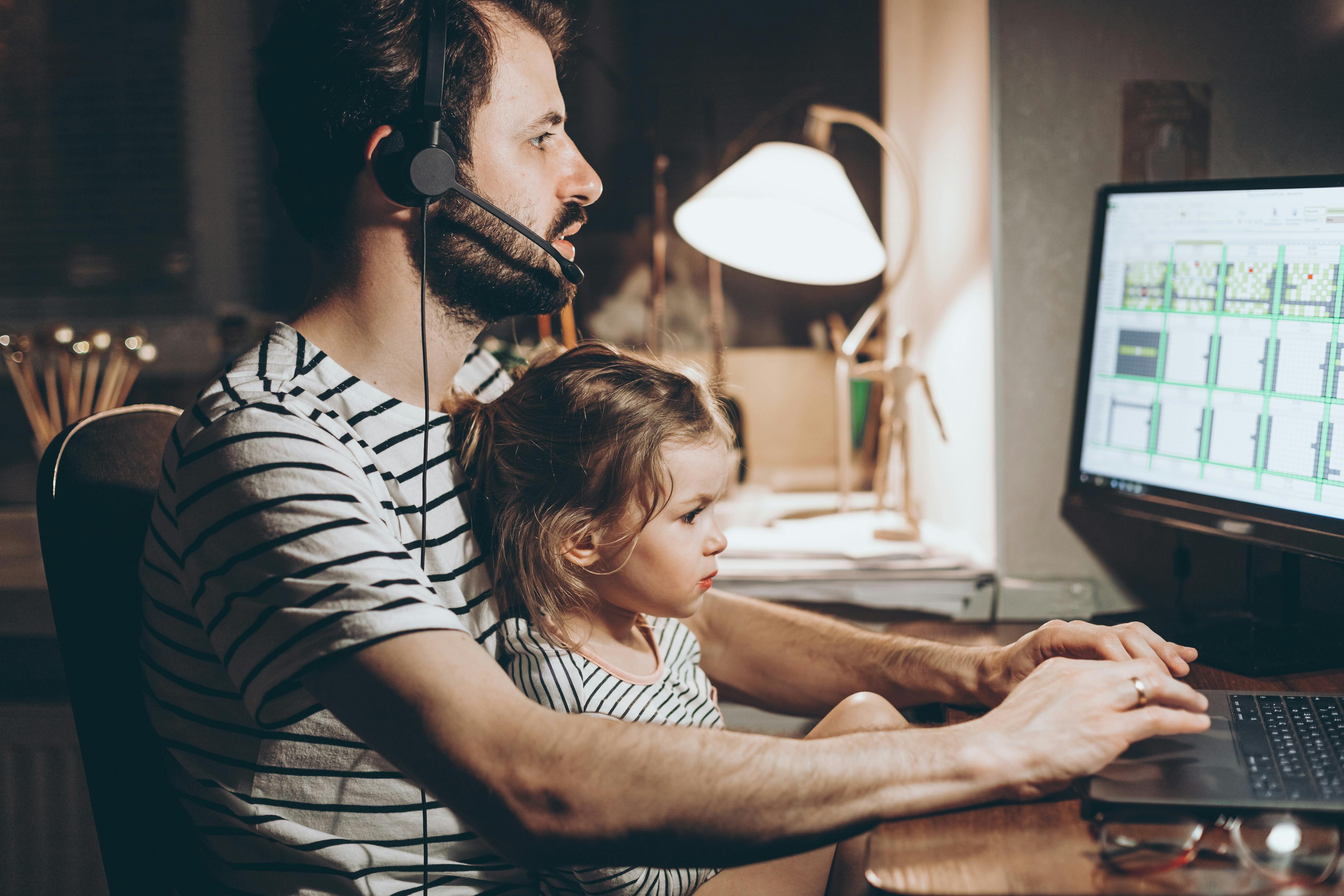 Un père travaille tard avec sa fille sur les genoux.