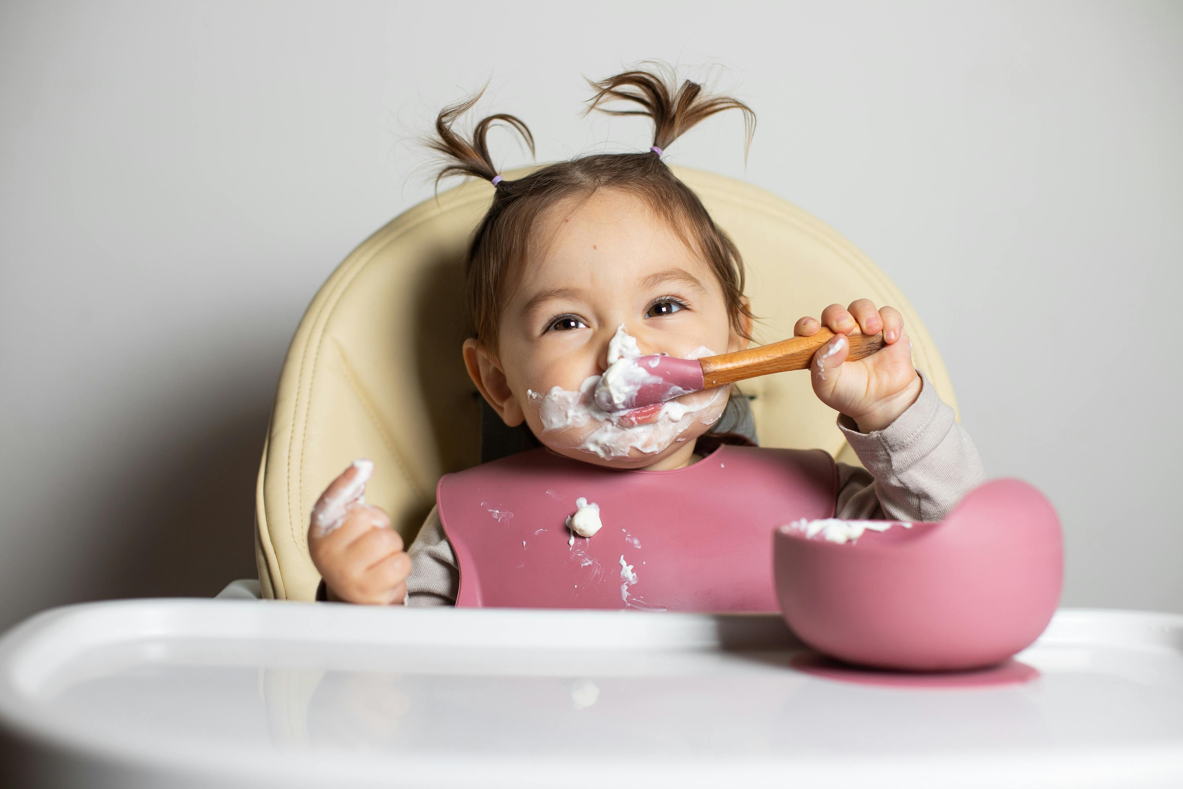 Un jeune enfant mange avec plaisir, se barbouillant de nourriture sur son visage, assis dans une chaise haute.