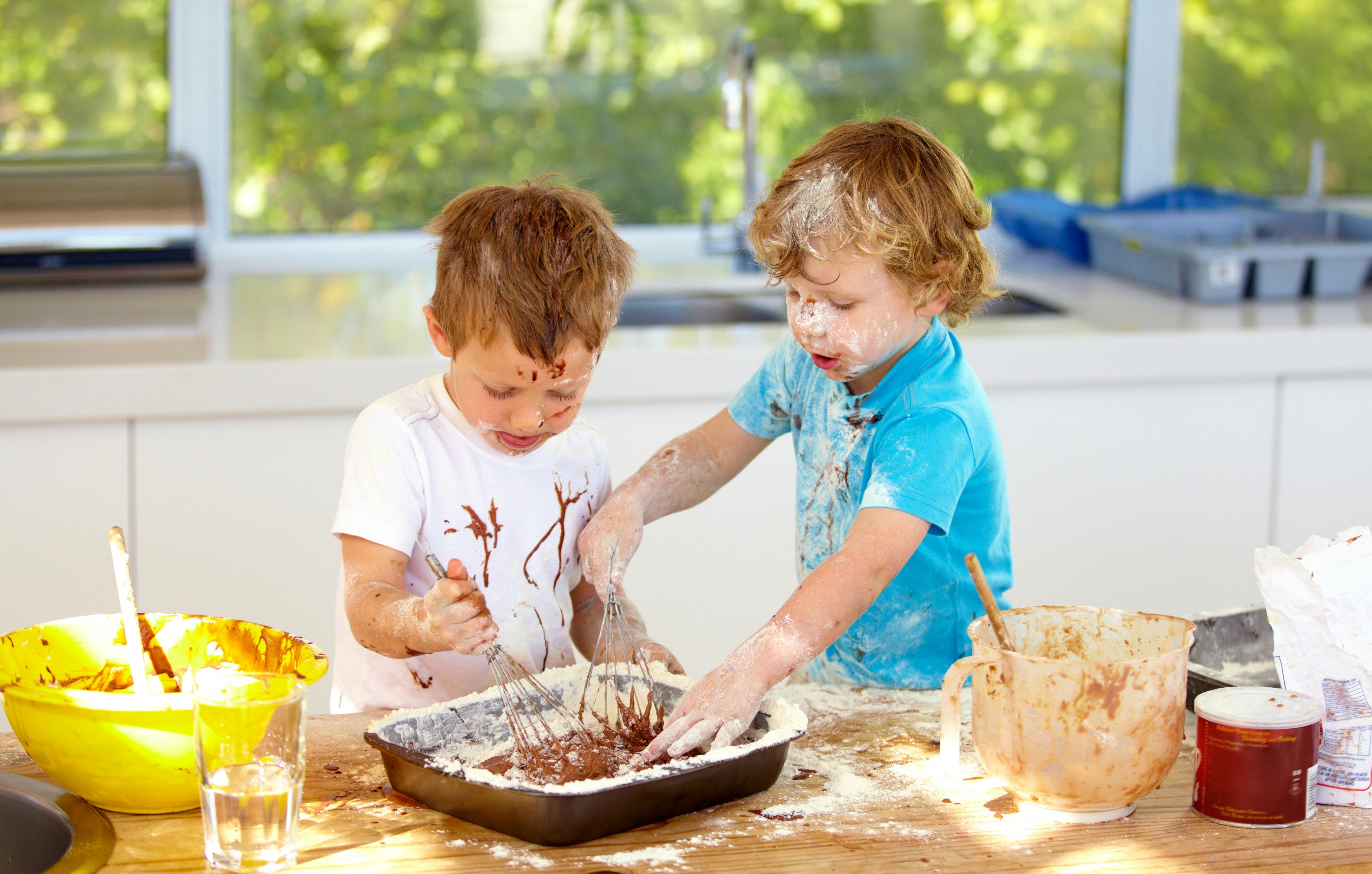 Deux garçons cuisinant dans une cuisine, recouverts de farine et de chocolat.