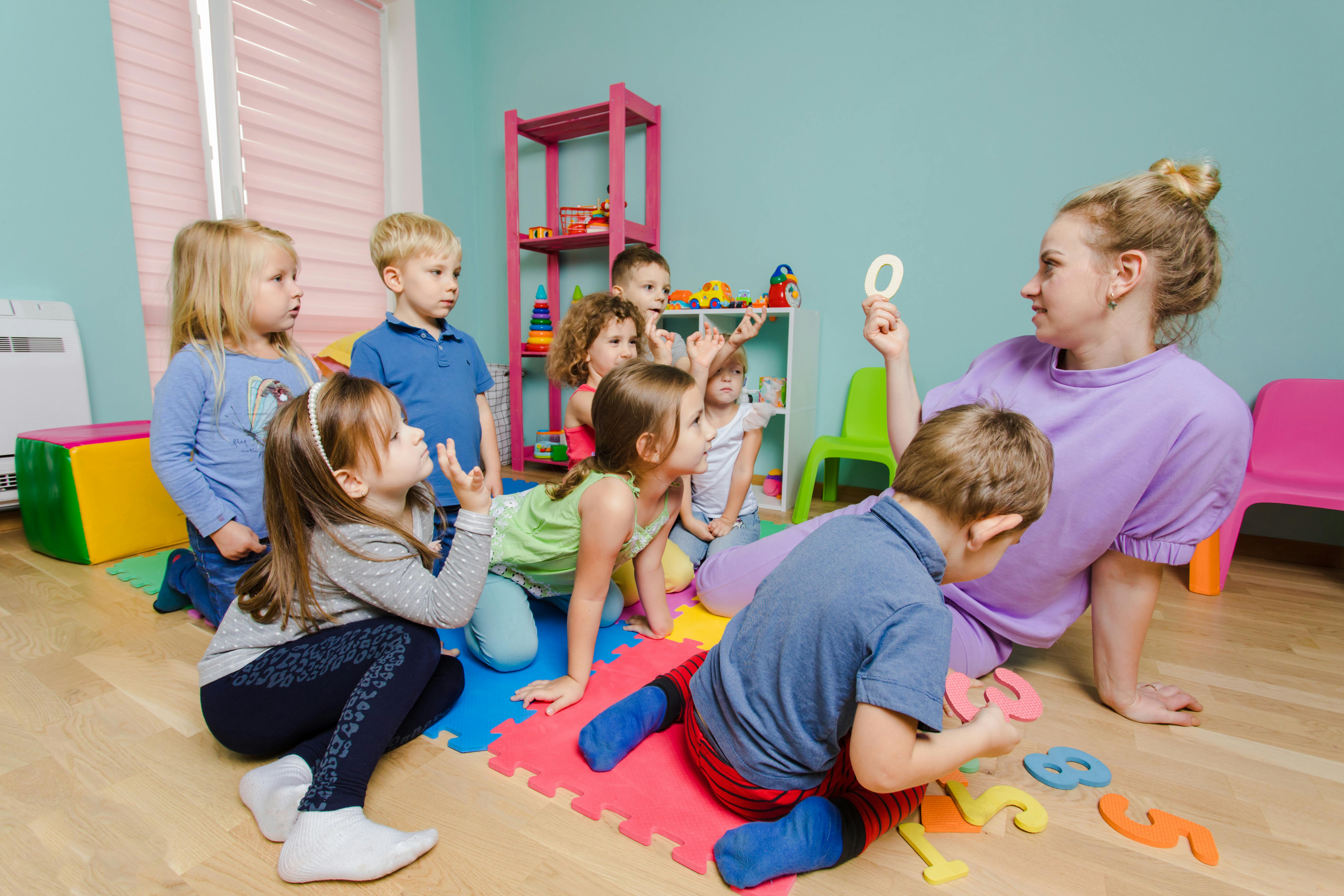 Une enseignante montre une lettre à un groupe d'enfants attentifs assis sur des tapis colorés.