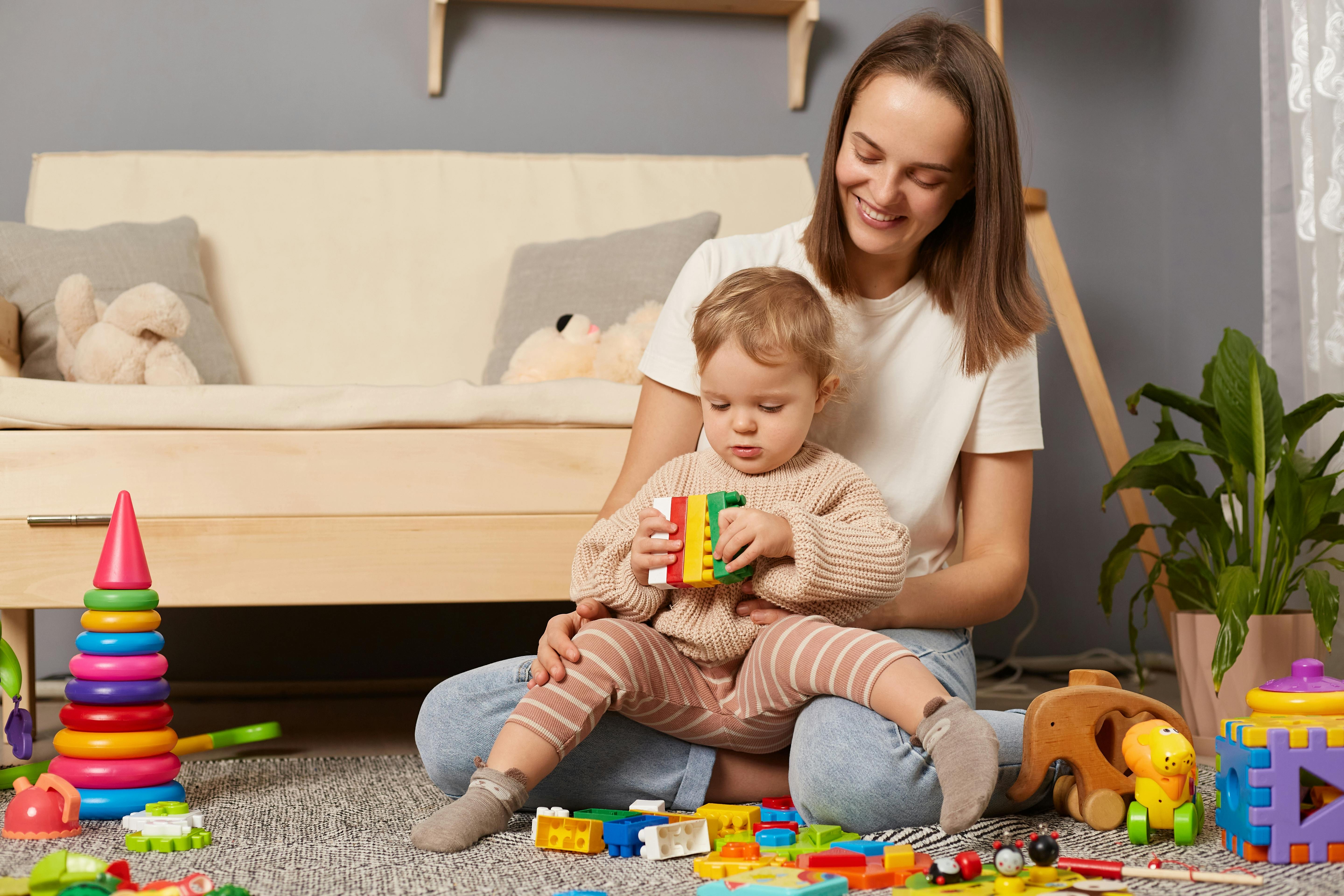 Une jeune mère tient sur ses genoux son bébé, en train de jouer avec de gros blocs de construction colorés.