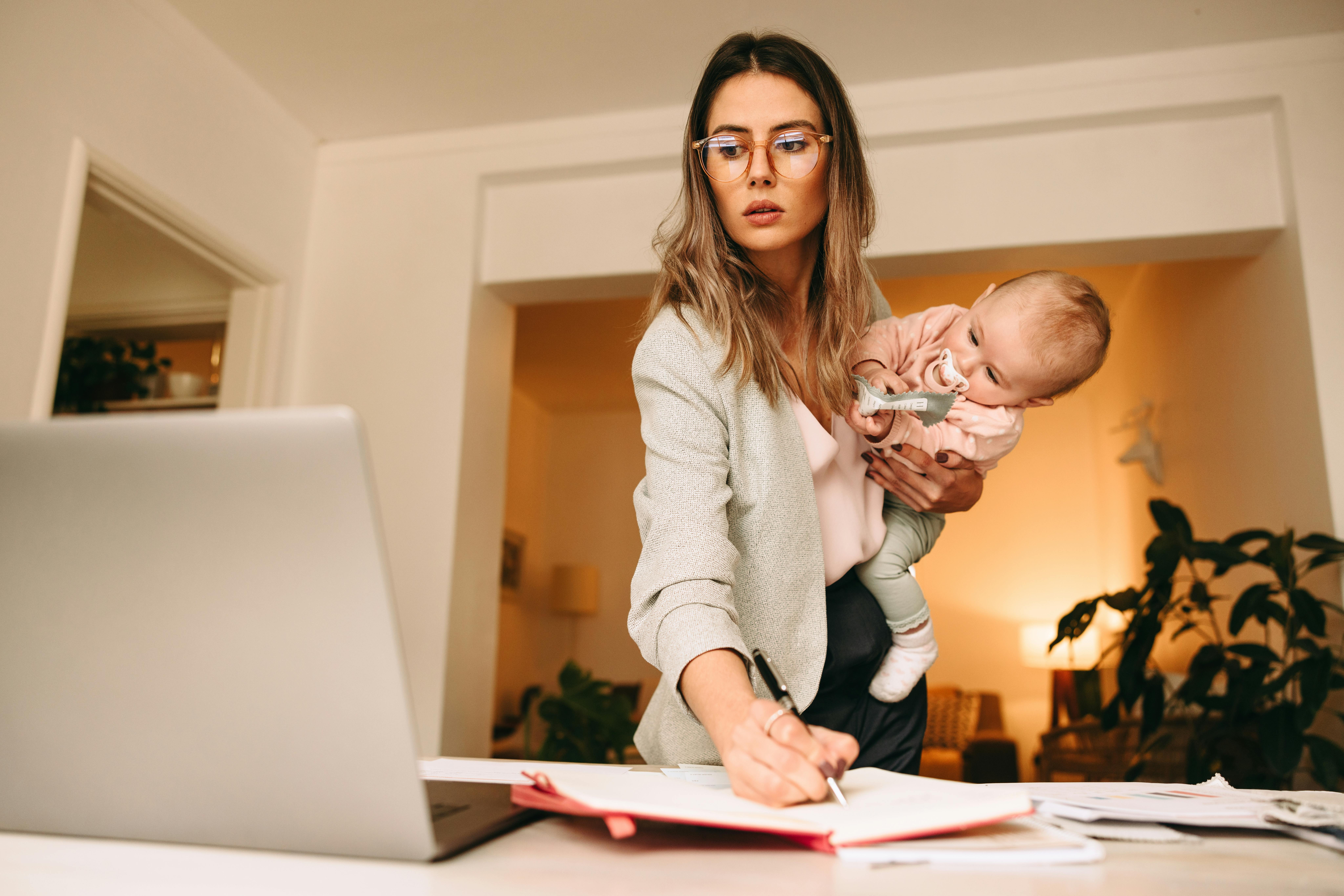 Une jeune femme active travaille en tenant son jeune bébé dans un bras, l'air inquiet.