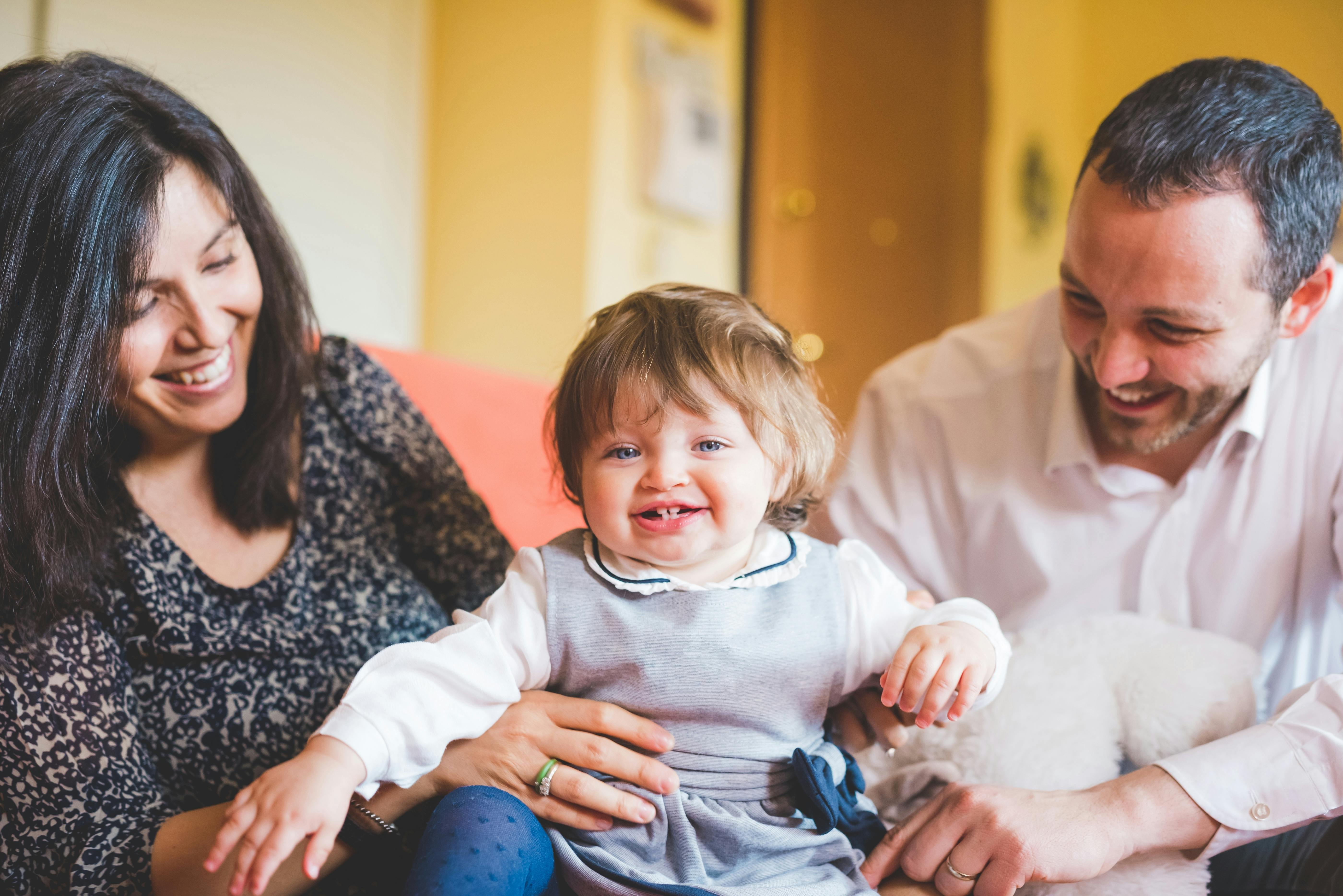 Une famille souriante avec un bébé assis entre les parents, tous les trois riant ensemble.