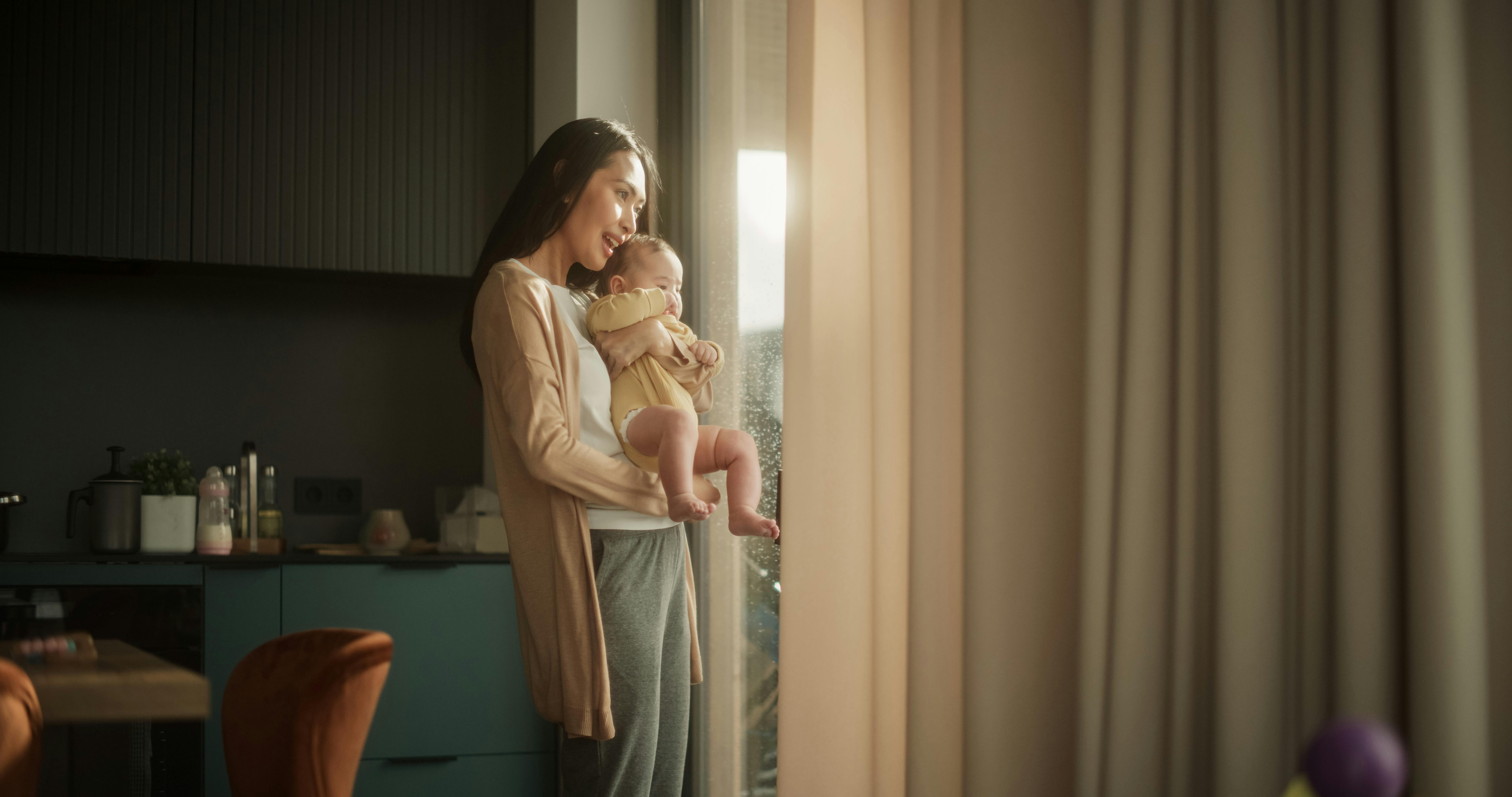 Une mère tenant son bébé et regardant par la fenêtre.