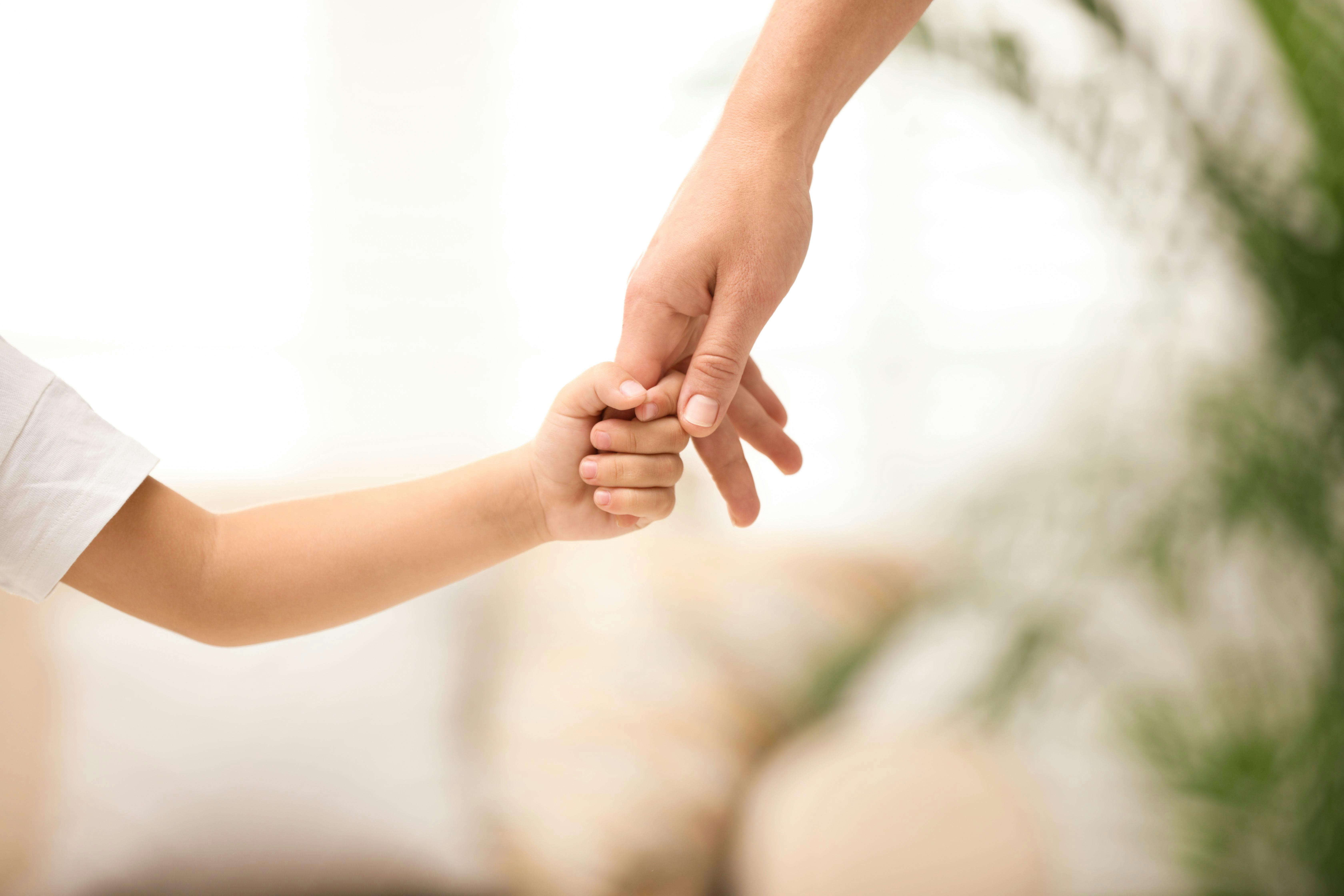 Une main d'adulte tenant la main d'un enfant.